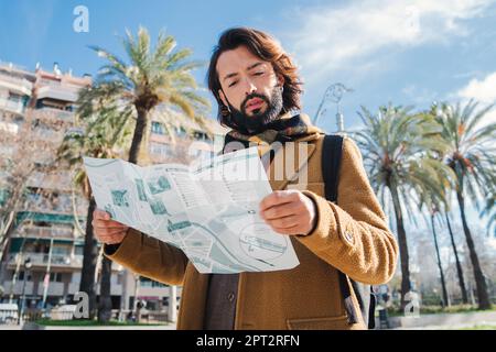 Portrait of bearded tourist male reading a map on Barcelona. Caucasian traveler guy sightseeing and searching locations on a guide. One young man lost on a journey trip in Spain looking the right way . High quality photo Stock Photo