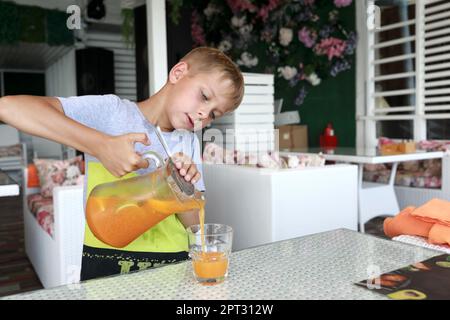 Boy pouring lemonade into glass in cafe Stock Photo