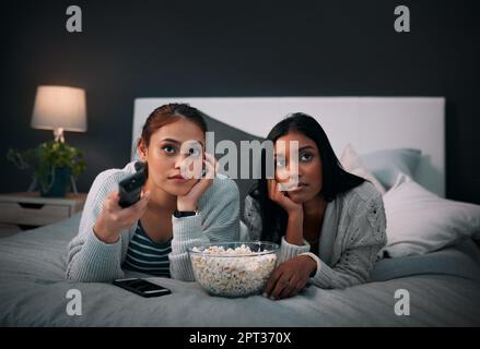 Not finding anything interesting to watch. two young women eating popcorn while watching a movie at home Stock Photo