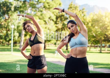 Breathe through it. two attractive young women stretching next to each other in the park during the day Stock Photo