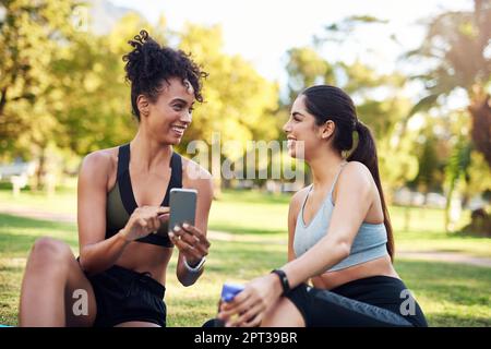 I think we deserve to take selfies. two attractive young women sitting next to each other while using a cellphone in the park Stock Photo