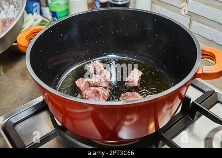 Diced beef meat is cooked in pot on gas stove. Stock Photo