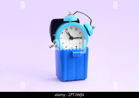Wasting time concept. Blue alarm clocks in plastic trash bin on violet background. Bad and wrong time management Stock Photo