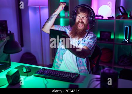 Young redhead man streamer playing video game using smartphone at gaming room Stock Photo