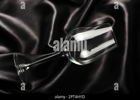 Empty wine glass lies on the black silk bed linen Stock Photo