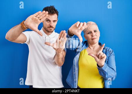 Young brazilian mother and son standing over blue background doing frame using hands palms and fingers, camera perspective Stock Photo