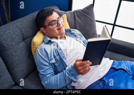 Down syndrome man reading book lying on sofa at home Stock Photo