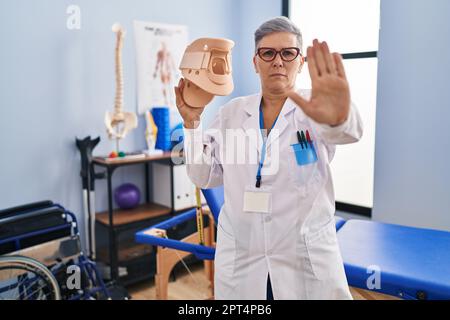 Middle age woman holding cervical neck collar with open hand doing stop sign with serious and confident expression, defense gesture Stock Photo