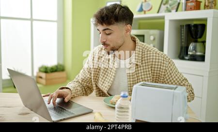 Young arab man having breakfast using laptop at home Stock Photo