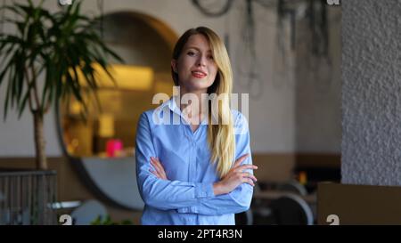 Beautiful young business lady looking at camera and smiling while standing indoors. Portrait of joyful pretty woman in restaurant. Successful Stock Photo