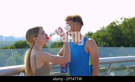 Cheerful Caucasian sporty people speaking and drinking water in city after exercising. Male and female athletes smiling and chatting in good mood Stock Photo