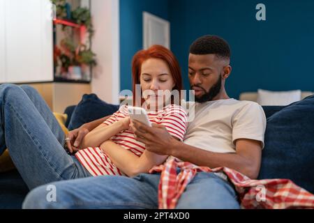 Young millennial diverse couple man and woman resting at home with mobile phone Stock Photo