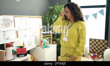 Middle age hispanic woman preschool teacher stressed standing at kindergarten Stock Photo