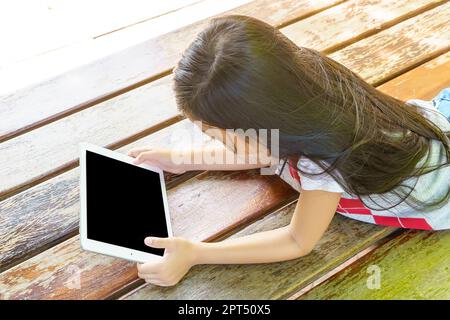 The girl lying on wooden bed with playing tablet pc. Stock Photo