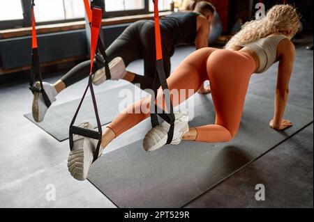 Athletic man woman doing crossfit training using trx equipment. Young female and male putting feet in stirrups Stock Photo