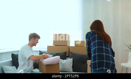 Caucasian joyful man and woman just moved in a new apartment packing their stuff and clothes. Cardboard boxes. Excited homeowners. Moving day. Happy Stock Photo