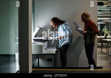 Zombie manager group in queue for copier at office. Exhausted worker copying paper document using printer-scanner Stock Photo