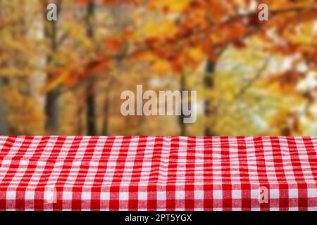Empty table product. Empty wooden deck table covered with a red white checkered tablecloth over abstract blurred autumn backdrop. Space for your food Stock Photo