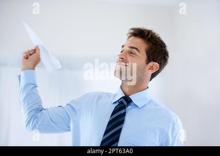 Playful in the workplace. A smiling businessman holding a paper plane and getting ready to throw it into the air Stock Photo