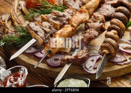 Various grilled meats. Shashlik from different meats on barbecue skewers with vegetables and lavash on wooden board. Top view. Food background. Servin Stock Photo