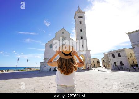 Holidays in Apulia, Italy. Back view of beautiful tourist woman holding her hat in Trani with its Cathedral in Apulia, Italy. Stock Photo