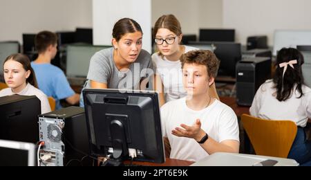 Two clever female students helping to male classmate while he is learning computer science in the computer room Stock Photo