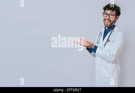 Handsome doctor showing an advertisement with his palms, Smiling doctor showing something with his palms. Young doctor presenting something with Stock Photo