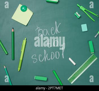 School supplies on empty green chalk board, top view. Chalk lettering back to school Stock Photo