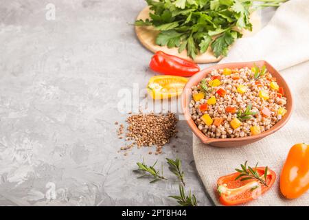 Buckwheat porridge with vegetables in clay bowl on a gray concrete background and linen textile. Side view, copy space. Russian traditional cuisine. Stock Photo