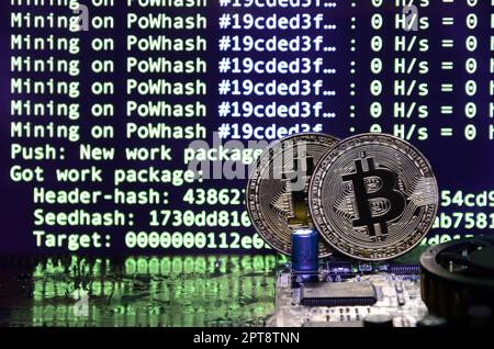 Two bitcoins lies on a videocard surface with background of screen display of cryptocurrency mining by using the GPUs Stock Photo