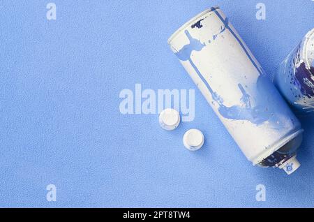 Some used blue aerosol spray cans and nozzles with paint drips lies on a blanket of soft and furry light blue fleece fabric. Classic female design col Stock Photo