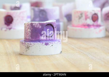 Several plastic nozzles from a paint sprayer that lie on a wooden surface against a gray wall background. The caps are smeared in violet paint. The co Stock Photo
