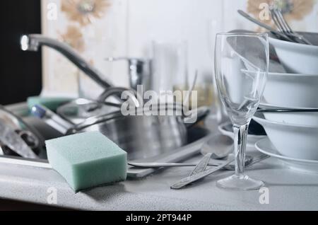A huge pile of unwashed dishes in the kitchen sink and on the countertop. A lot of utensils and kitchen appliances before washing. The concept of dail Stock Photo