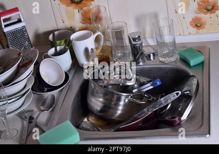 A huge pile of unwashed dishes in the kitchen sink and on the countertop. A lot of utensils and kitchen appliances before washing. The concept of dail Stock Photo