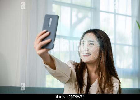 Asian women use smartphone for access control face recognition in private identification on sofa living room at home, Asian female checking her person Stock Photo