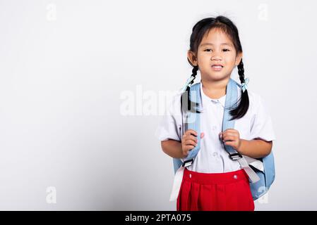 Asian adorable toddler smiling happy wearing student thai uniform red skirt standing in studio shot isolated on white background, Portrait little chil Stock Photo