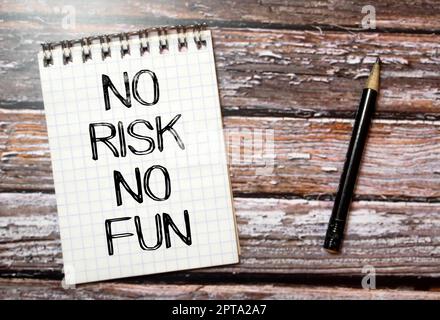 yellow self-adhesive note sticker diagonally on a dark wooden table top with stylized handwriting with the text: no risk no fun Stock Photo