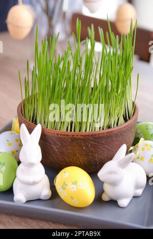 Home easter decor. Green oats, decorative rabbits and eggs on table near white brick wall Stock Photo
