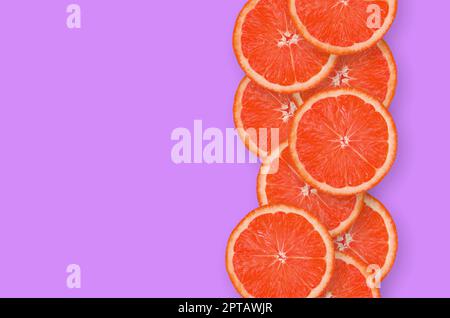 Top view of grapefruit fruit slices on bright purple background. A saturated citrus vertical row with copy space. Minimalistic flat lay Stock Photo