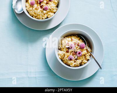 Quinoa porrige on tabletop. Two bowl wit quinoa milk porridge with berries and almond. Frozen raspberries in quinoa porrige Stock Photo