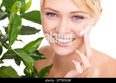 Nature enhances her beauty. A beautiful young woman applying moisturizer to her face while surrounded by leaves Stock Photo