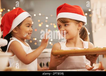 Playful bakers. Two little girls wearing santa hats baking in the kitchen Stock Photo