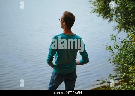 Rear view of a man standing on the shore of a lake and looking at the water Stock Photo