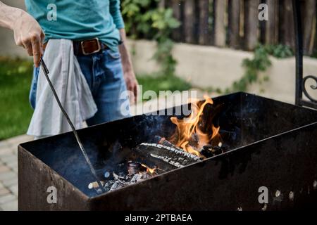 Unrecognizable man stirs the coals in the grill Stock Photo