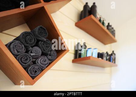 Shelves with rolled towels and professional hair cosmetics on wall