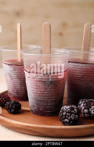 Tasty blackberry ice pops in plastic cups on white table, closeup. Fruit popsicle Stock Photo
