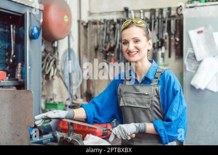 Female worker in metal workshop looking at camera being surrounded by work tools Stock Photo