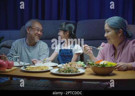 Happy Asian family grandparent and granddaughter dining on table and having fun during at house evening time, Happiness senior parent and child eating Stock Photo