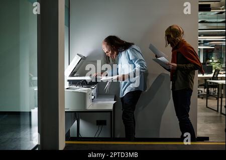 Zombie manager group in queue for copier at office. Exhausted worker copying paper document using printer-scanner Stock Photo