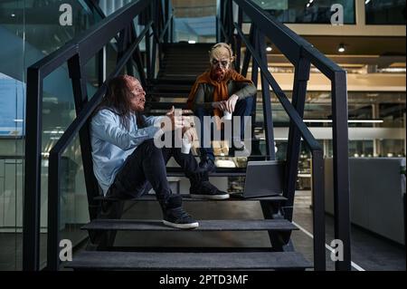 Zombie workers drinking coffee chatting sharing idea on staircase enjoy rest during work break. Office open space Stock Photo
